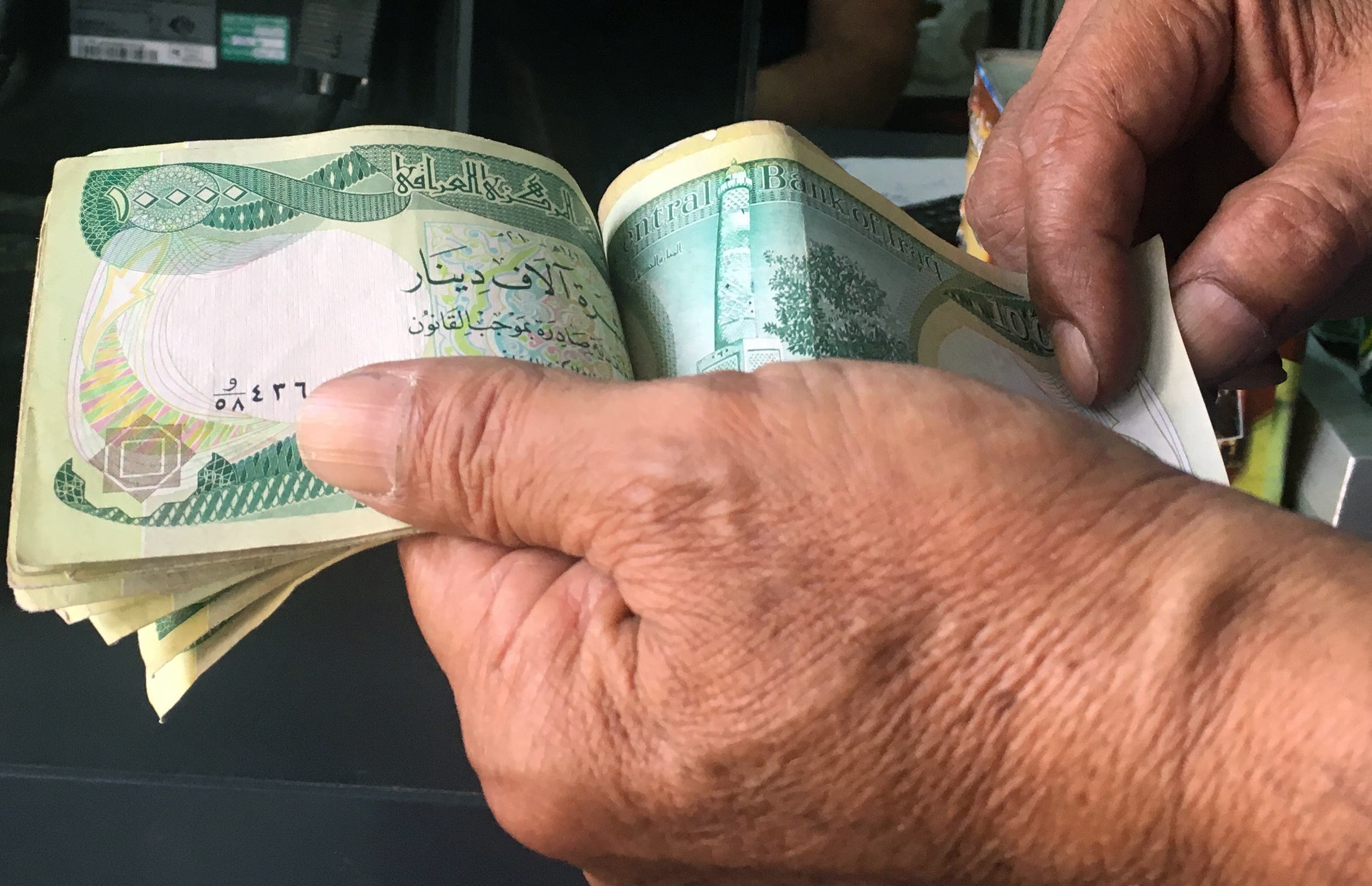 An Iraqi policeman pays for groceries with 10,000-Iraqi dinar banknotes bearing an image of Mosul's iconic leaning minaret, known as the Hadba (Hunchback), on June 22, 2017, in the capital Baghdad. (AFP)