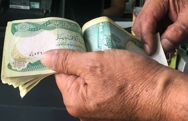 An Iraqi policeman pays for groceries with 10,000-Iraqi dinar banknotes bearing an image of Mosul's iconic leaning minaret, known as the Hadba (Hunchback), on June 22, 2017, in the capital Baghdad. (AFP)