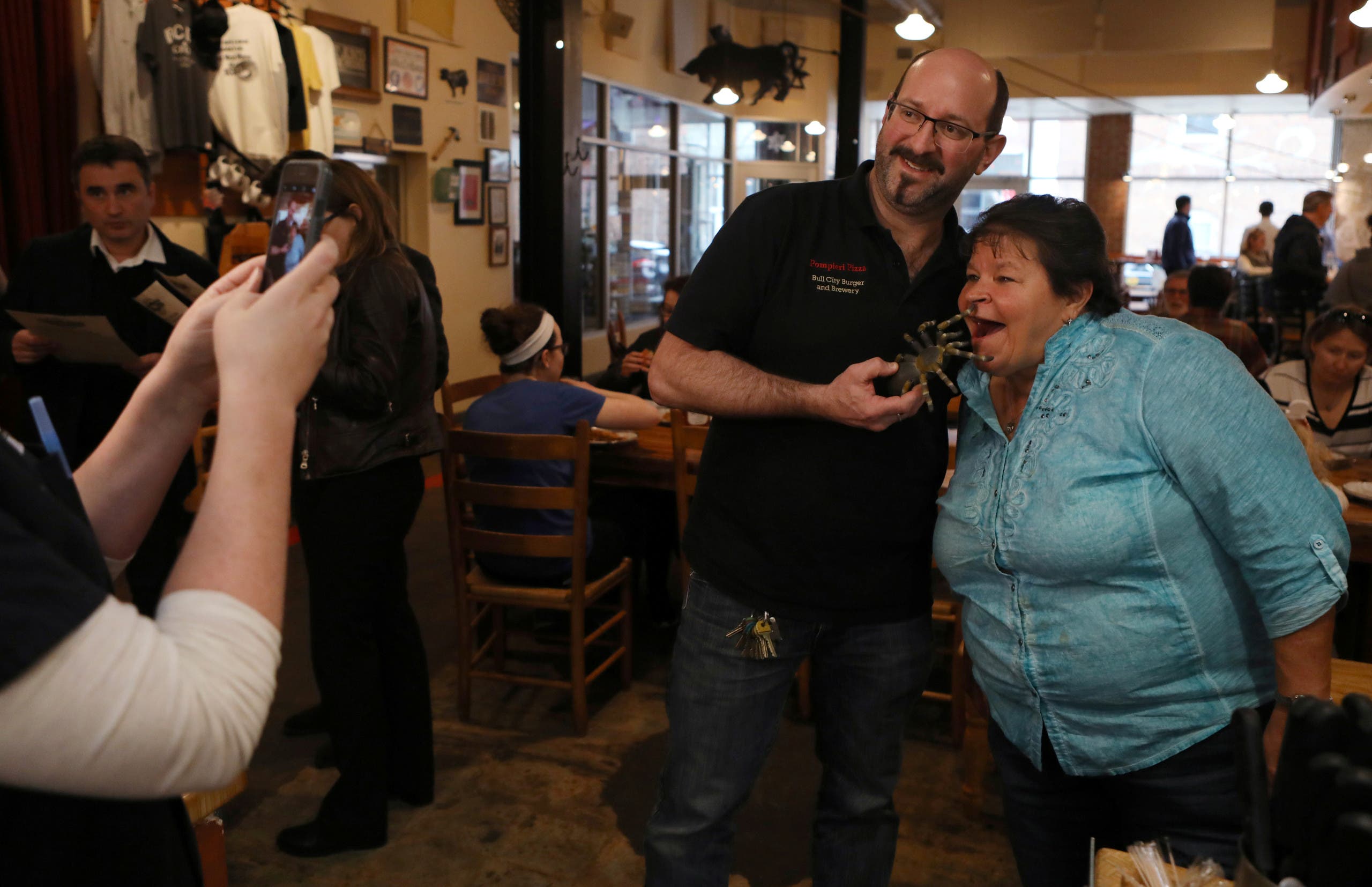 Bull City Burger and Brewery owner Seth Gross posses with a customer as he holds a tarantula toy before the restaurant serves their tarantula burger to another customer in celebration of Exotic Meat Month in Durham, North Carolina, U.S. April 16, 2018. Picture taken April 16, 2018. REUTERS/Jim Urquhart