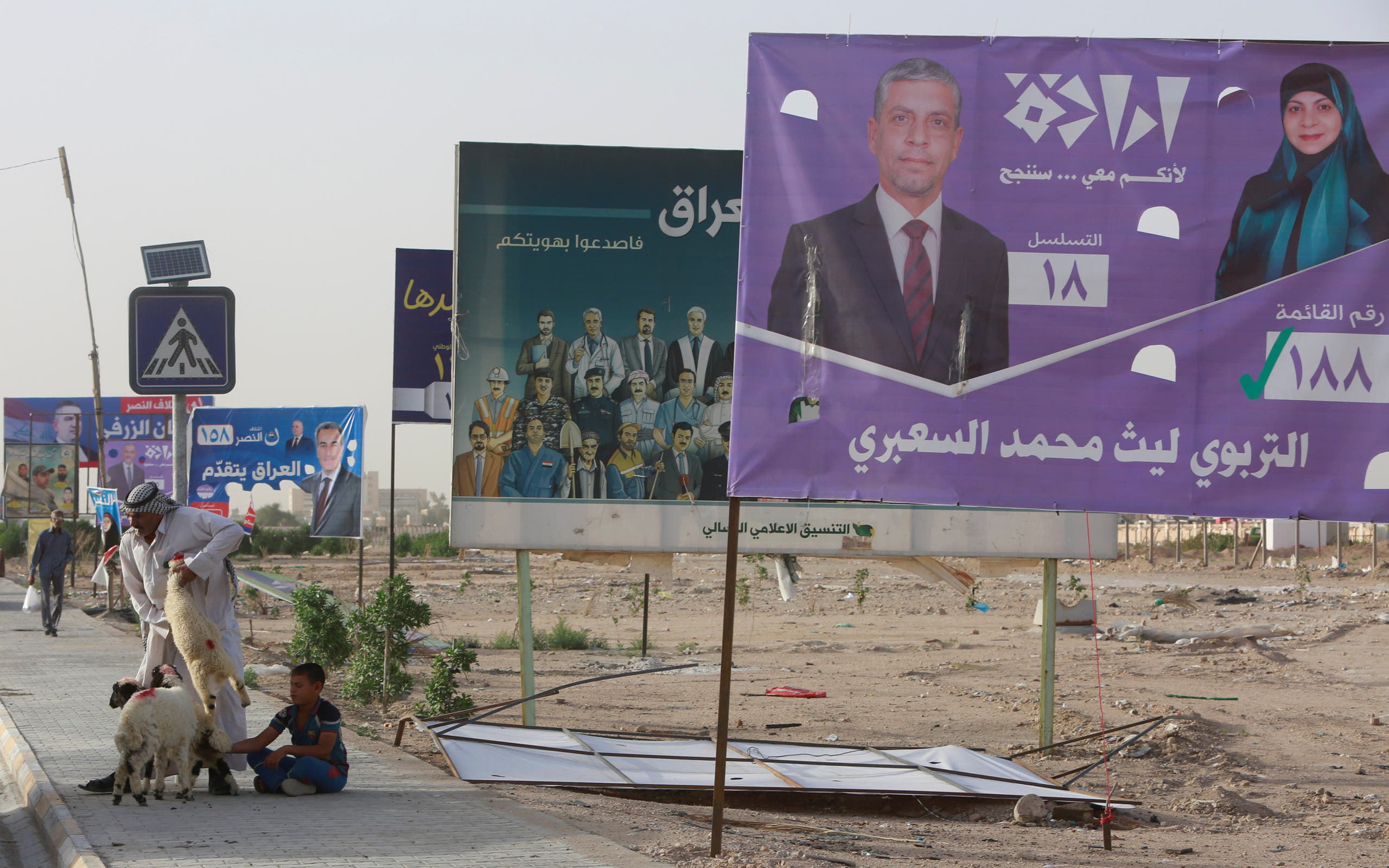 A man holds a sheep for sale next to campaign posters of candidates ahead of parliamentary election, in Iraq, April 20, 2018. (Reuters)