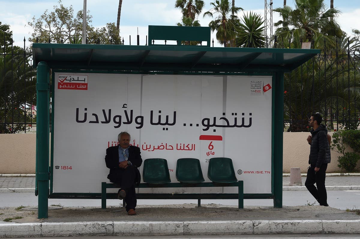 A tunisian man waits for a bus in front of a municipal elections awareness campaign poster in Tunis. (AFP)