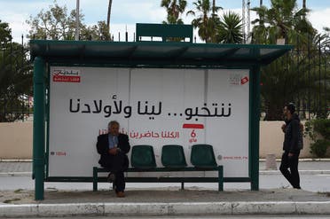 A tunisian man waits for a bus in front of a municipal elections awareness campaign poster in Tunis. (AFP)