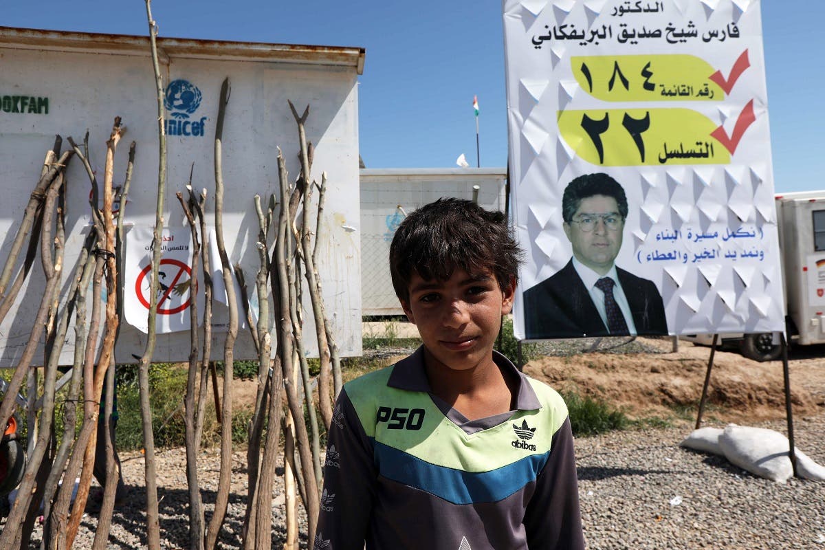 A displaced Iraqi from the former embattled city of Mosul poses for a photo in front of an election campaign poster, at the Hasan Sham camp. (AFP)