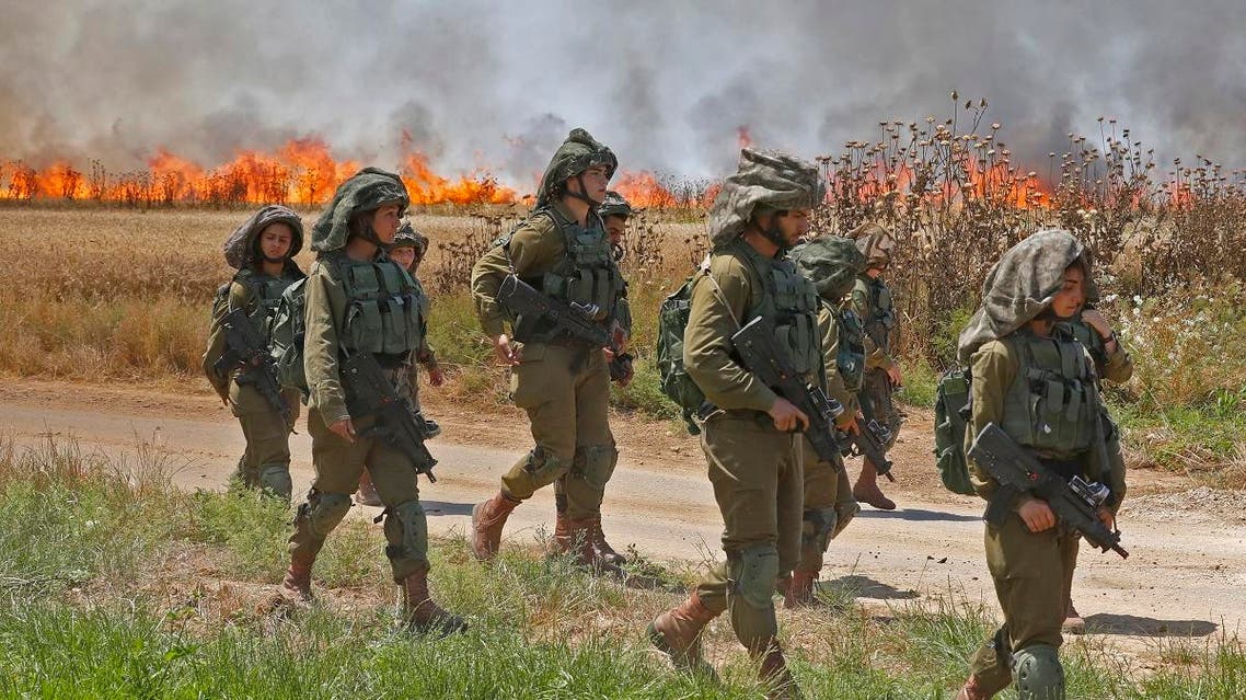 Israeli soldiers walk amidst smoke from a fire in a wheat field near the Kibbutz of Nahal Oz, along the border with the Gaza. (AFP)