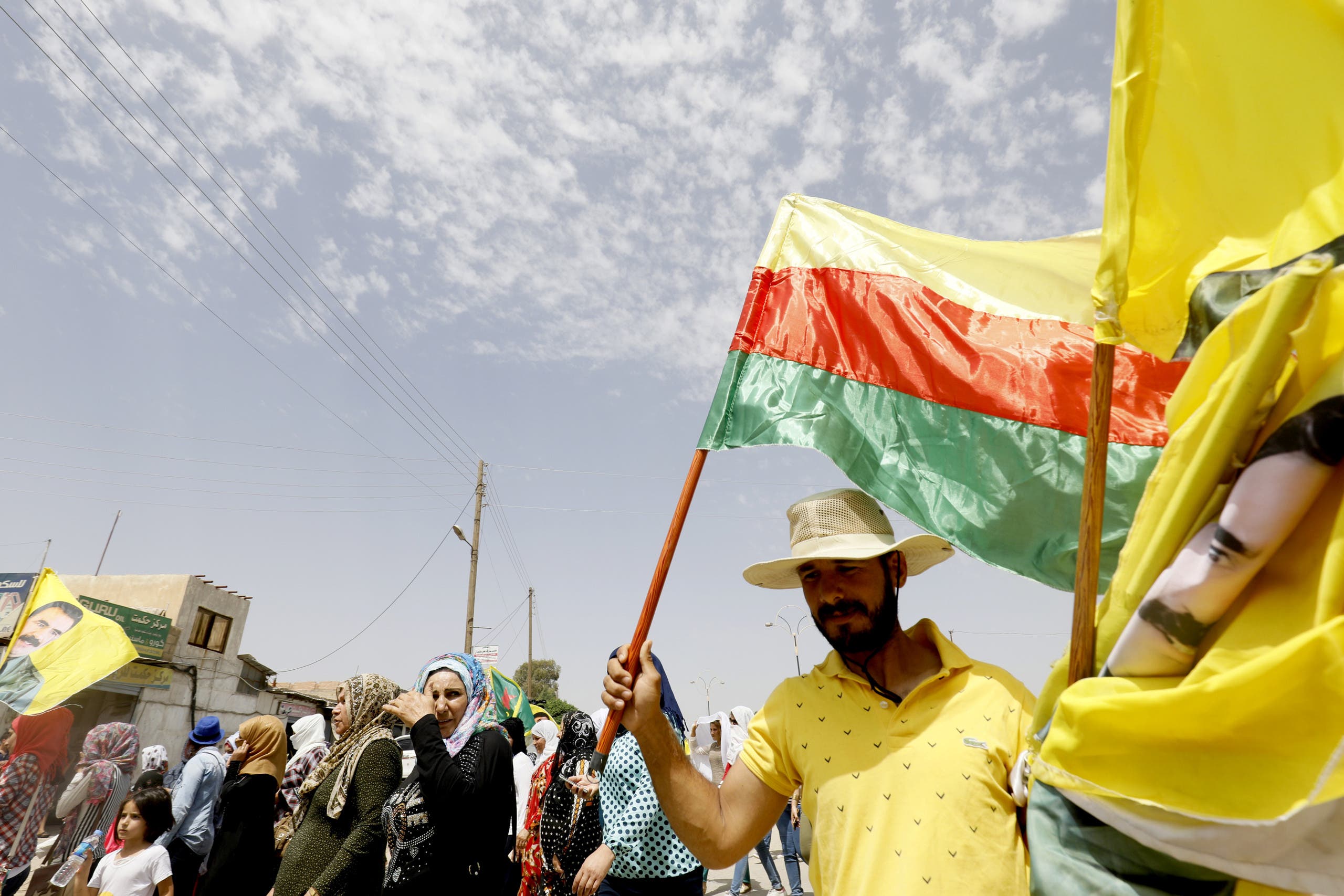 A Syrian-Kurdish man holds a Kurdish flag as well as flags with the face of Kurdistan Worker's Party (PKK) leader Abdullah Ocalan as people demonstrate against demographic changes forced by Turkey to repopulate Kurdish areas, in Qamishli on May 26, 2018. Delil souleiman / AFP