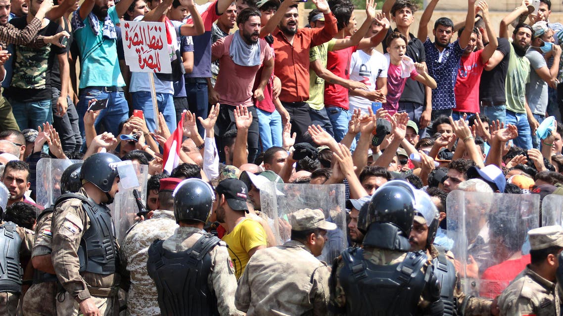 Iraqi riot police lined up as protesters chant slogans and hold up signs during a demonstration in Basra on July 15, 2018. The arabic sign in red at top left reads:"Basra oil for Basra". Dozens of demonstrators were wounded in southern Iraq today in clashes with police as protests over unemployment and a lack of basic services entered a second week, officials said.