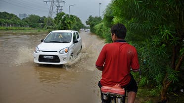 An Indian youth on a bicycle waits for a car to pass as he negotiates his way through a flooded road following monsoon rains in Greater Noida, India, Friday, July 27, 2018. (AP)
