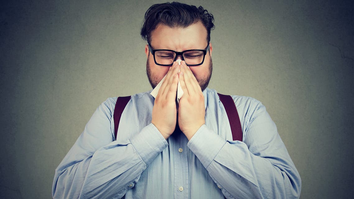 Sneezing chunky man posing on gray - Stock image