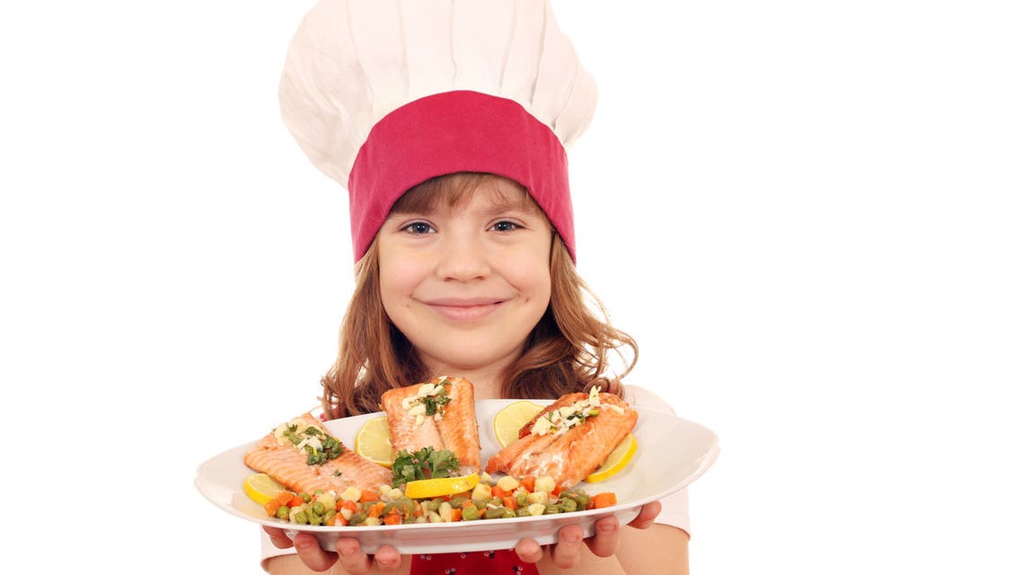Happy little girl cook hold plate with salmon seafood - Stock image