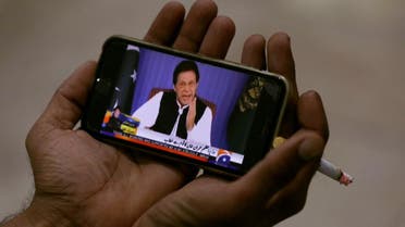 Journalist poses with a cell phone displaying Imran Khan speaking in his first televised address. (Reuters)