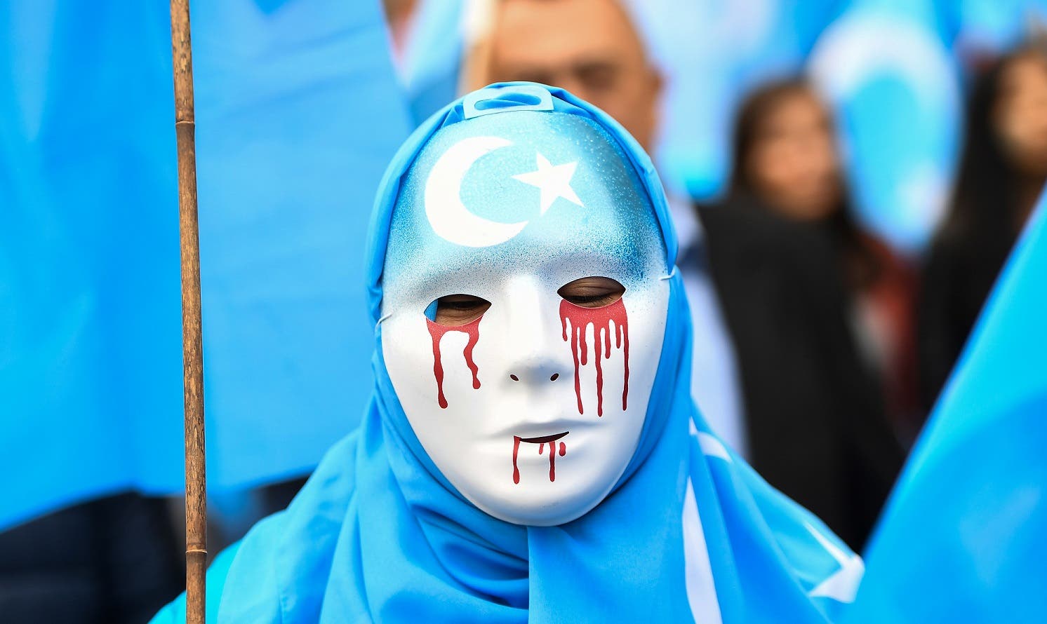A person wearing a white mask with tears of blood takes part in a protest march in Brussels in support of ethnic Uighurs. (AFP)