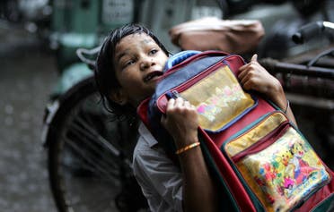 A young student struggles to lift up her school under rains in New Delhi on July 4, 2007. (File photo: AP)