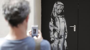 In this file photo taken on June 25, 2018, a man takes a photograph of an artwork by street artist Banksy in Paris on a side street to the Bataclan concert hall where a terrorist attack killed 90 people on Novembre 13, 2015. (AFP)