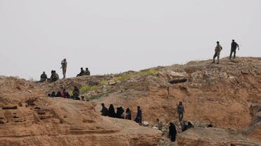 Fighters of SDF stand near ISIS fighters and their families who surrendered in the village of Baghouz. (Reuters)