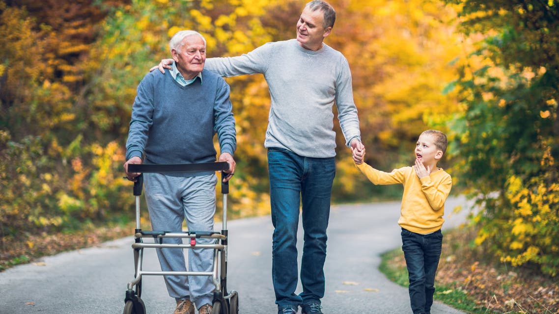 Elderly father adult son and grandson out for a walk in the park. - Stock image