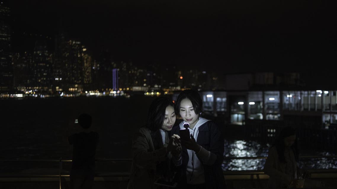 Two women look at a mobile phone after the skyline buildings lights were switched off for Earth Hour in Hong Kong on March 24, 2018. (AFP)