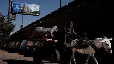 In this Oct. 28, 2018 photo, a man on a donkey cart makes his way under a residential billboard advertisement for a gated compound, near a wall that separates the ring road from slum area Ezbet Khairallah, in Cairo, Egypt. (AP)