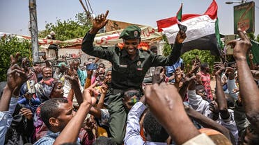 A Sudanese soldier joins protestors shouting slogans and waving national flags during a protest outside the army complex in the capital Khartoum on April 18, 2019. (AFP)