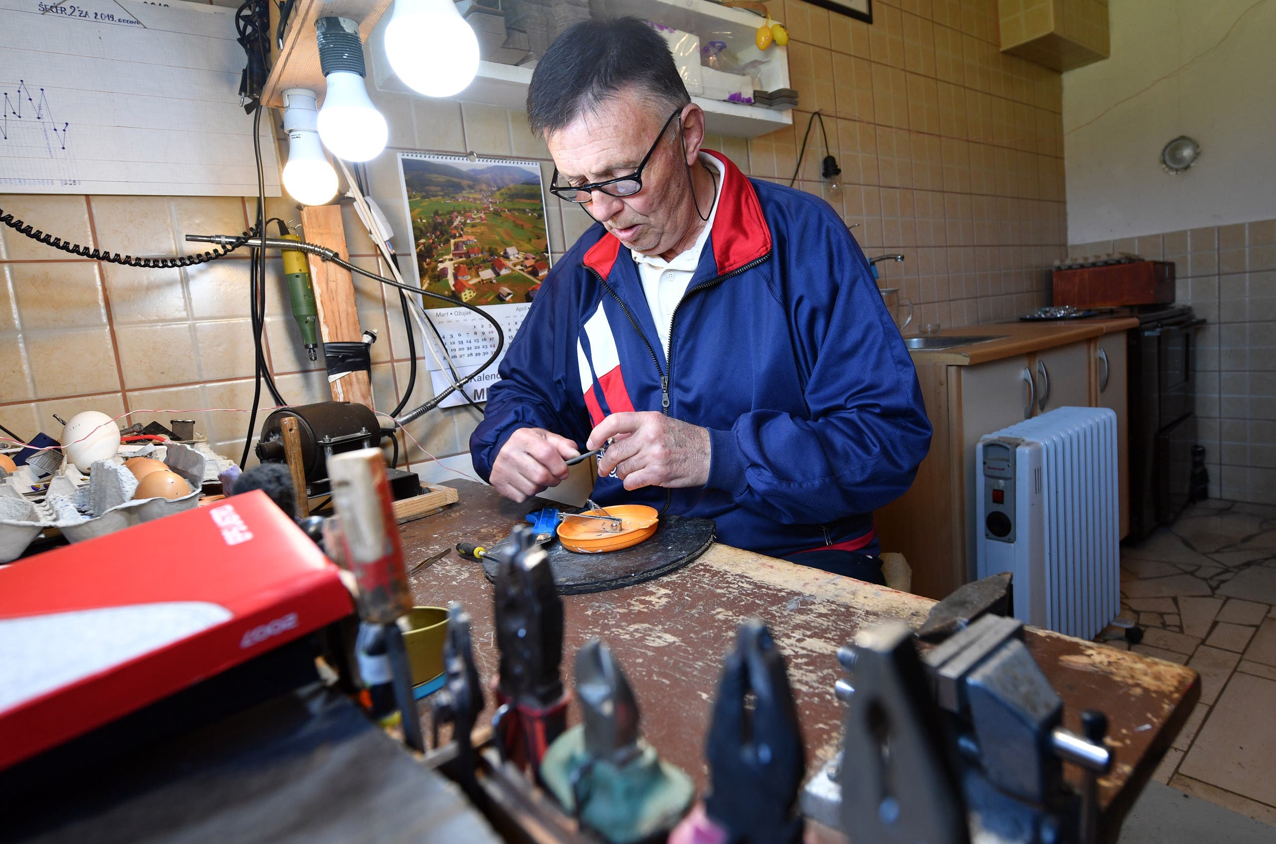 Stjepan Biletic, 71, handcrafts man from Central-Bosnian town of Kresevo, nails miniature horseshoe onto an egg, in his workshop, on April 17, 2019.(AFP)