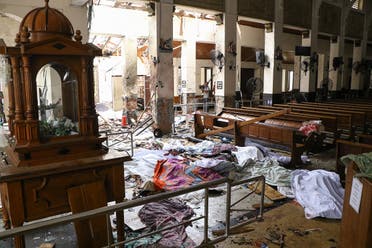 Sri Lankan security personnel walk past dead bodies covered with blankets amid blast debris at St. Anthony's Shrine. (AFP)