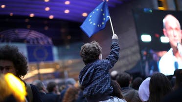 A young boy waves an EU flag as he watches a giant screen television outside the European Parliament in Brussels, Sunday, May 26, 2019. (AP)