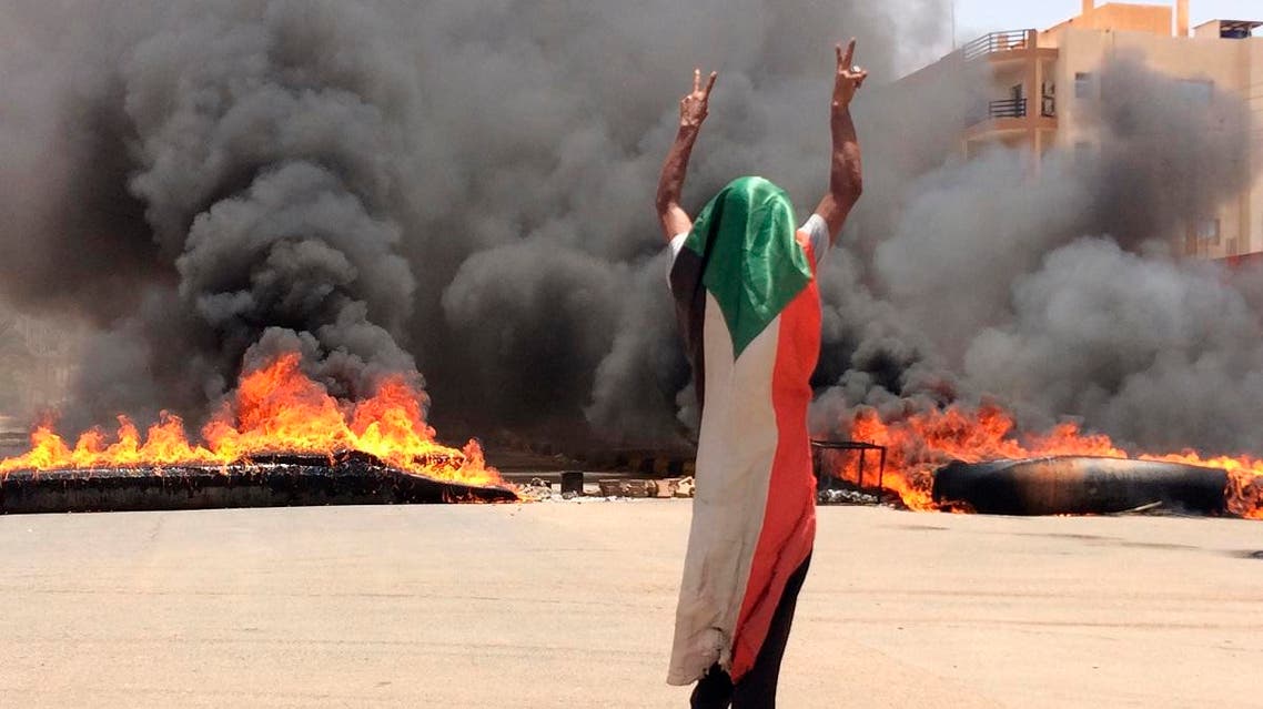 A protester wearing a Sudanese flag flashes the victory sign in front of burning tires and debris on road 60, near Khartoum's army headquarters in Khartoum, Sudan, Monday, June 3, 2019. (AP)