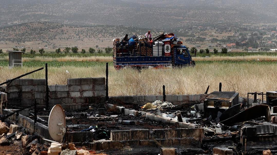 A Syrian family with their belongings ride past a burnt tent in a truck as they evacuate the informal refugee camp in Deir al-Ahmar, east Lebanon, Sunday, June 9, 2019. (AP)