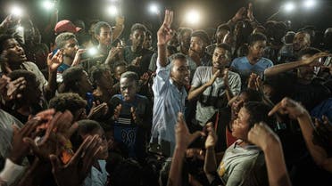 People chant slogans as a young man recites a poem, illuminated by mobile phones, before the opposition’s direct dialogue with people in Khartoum on June 19, 2019. (AFP)