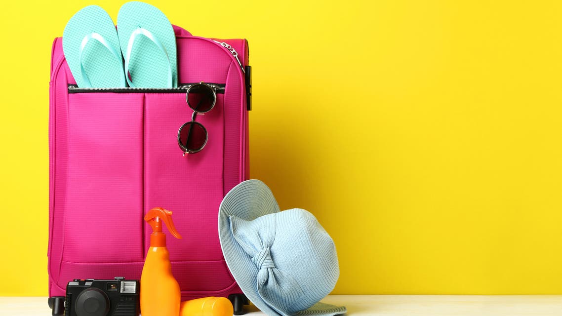 Pink suitcase with flip-flops, hat, sunglasses and sunscreen bottles on wooden table stock photo