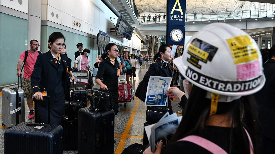 Cabin crew walk past a protester handing out leaflets and chanting slogans as protesters rally against a controversial extradition bill in the arrivals hall of the international airport in Hong Kong on July 26, 2019. (AFP)