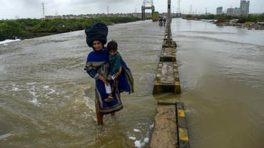 A woman holds her baby as she crosses a flooded street after heavy monsoon rains in Karachi on August 1, 2019. (AFP)