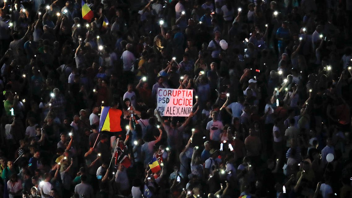 People flash the light of their mobile phones and hold a banner that reads "Corruption Kills" during an anti-government protest in Victoria Square, outside the government headquarters in Bucharest, Romania, Saturday, Aug. 10, 2019. (AP)