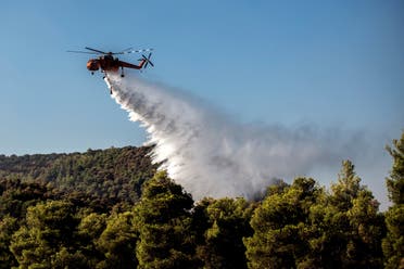 A firefighting helicopter drops water over a fire near the village of Makrimalli on the island of Evia, northeast of Athens. (AFP)