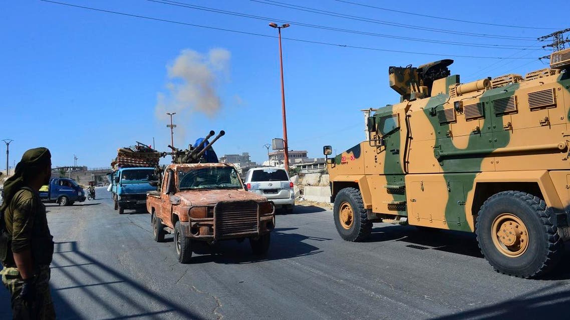 Smoke rises in the background from bombardment around the area as fighters with the Free Syrian army drive their pick-up truck, left, past a Turkish Armed Forces convoy. (AFP)