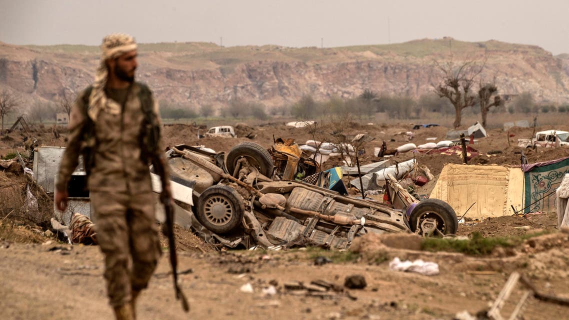 A member of the Syrian Democratic Forces (SDF) walks past damaged vehicles on the side of a road in the village of Baghouz in Syria's eastern Deir Ezzor province near the Iraqi border on March 24, 2019, a day after the Islamic State (IS) group's caliphate was declared defeated by the US-backed Kurdish-led Syrian Democratic Forces (SDF).