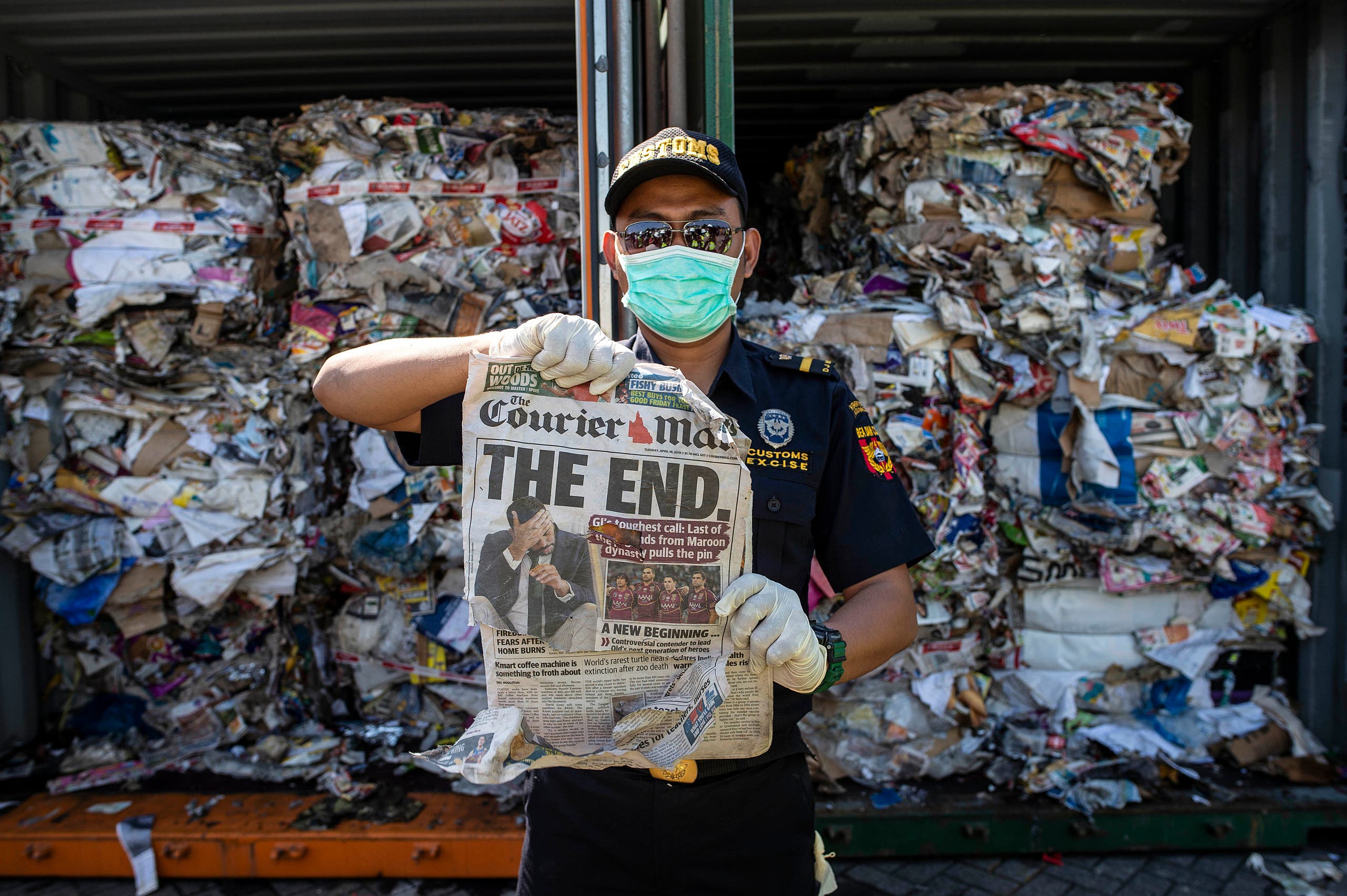 An Indonesian customs officer holds up a newspaper from a container filled with trash originating from Australia, which should have contained only waste paper, but authorities also found hazardous material and household trash, at a port in Surabaya on July 9, 2019. (AFP)