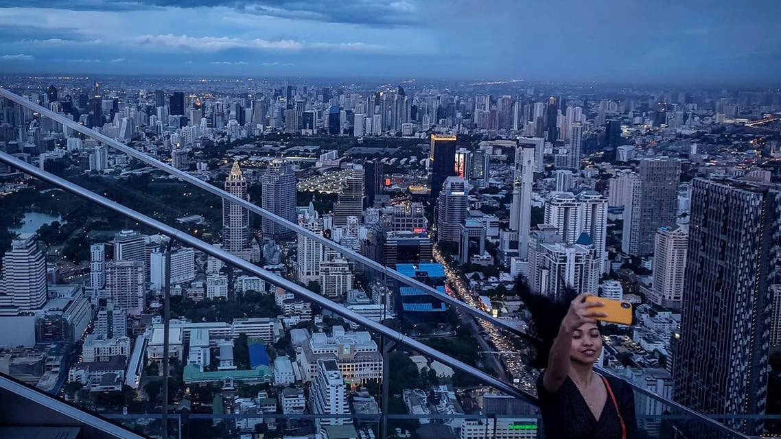 This picture taken on June 26, 2019 shows a tourist taking a selfie photograph in front of the city skyline from the Mahanakorn Skywalk's observation deck area, located 314 metres above the ground, in Bangkok. (AFP)