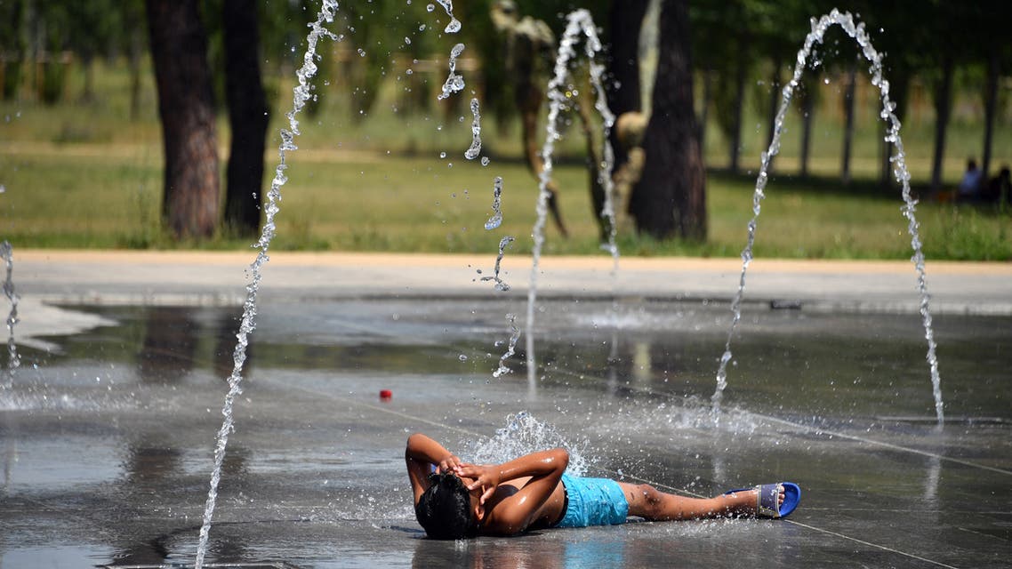 (FILES) In this file photo taken on June 27, 2019 a boy lies on the pavement as he cools off under water jets at a fountain in Montpellier southern France, during a heat wave. In June and July 2019 in France, around 1.500 more people died than usual due to heatwaves, according to a French Ministry of Health study released on September 8, 2019.