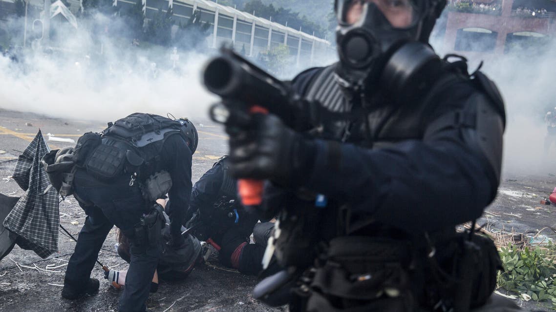 A riot police officer points his projectile launcher as his colleagues detain demonstrators in the Sha Tin district of Hong Kong on October 1, 2019 (AFP)
