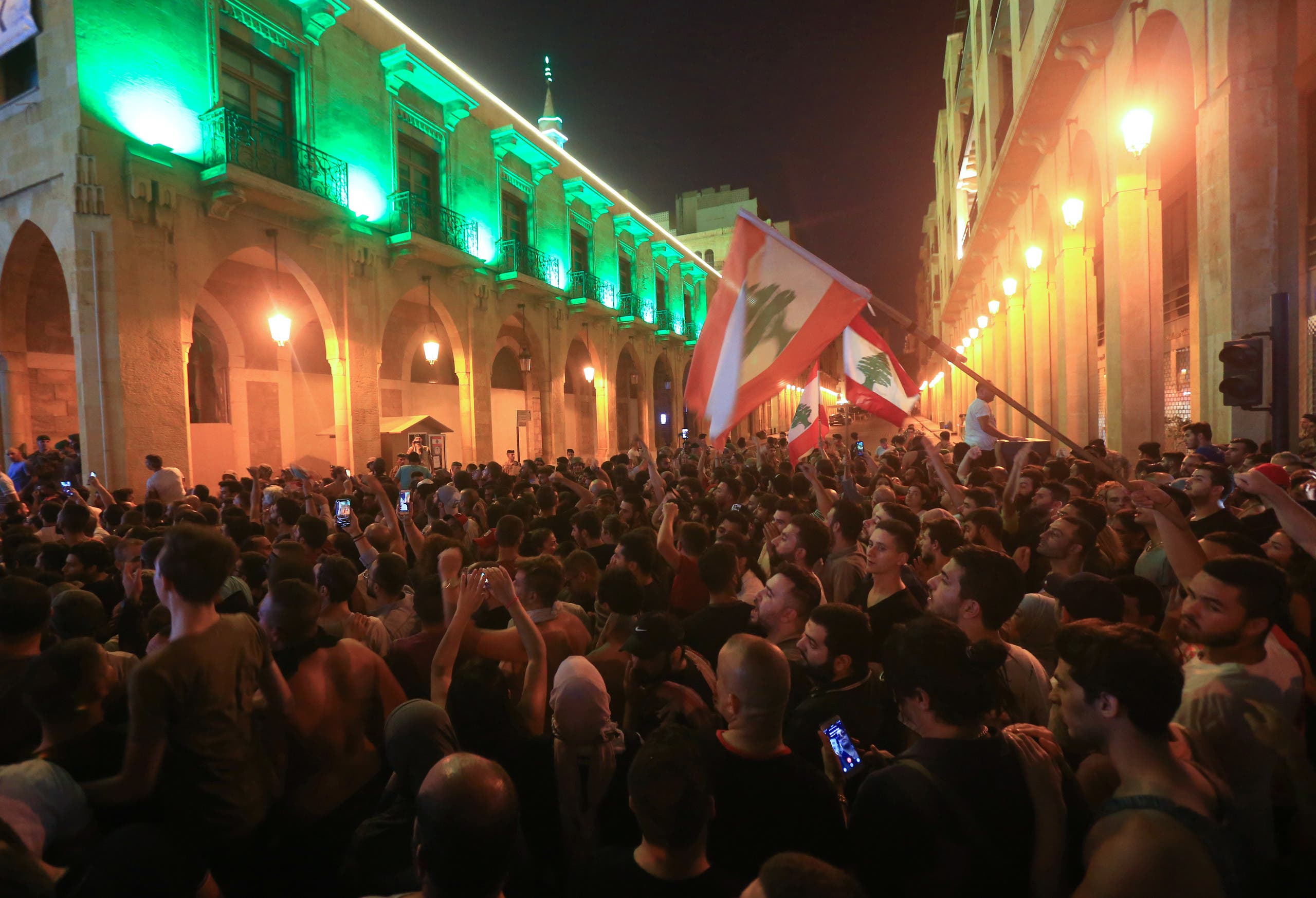 Demonstrators wave flags during a protest against a government decision to tax calls made on messaging applications on October 17, 2019 outside the government palace in Beirut. (AFP)