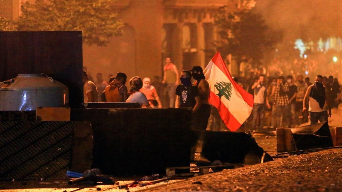 Lebanese demonstrators stand with a national flag behind a make-shift barricade amidst clashes with security forces during a mass protest at Riad al-Solh Square in the centre of the capital Beirut on October 18, 2019 against dire economic conditions. (AFP)