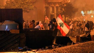 Lebanese demonstrators stand with a national flag behind a make-shift barricade amidst clashes with security forces during a mass protest at Riad al-Solh Square in the centre of the capital Beirut on October 18, 2019 against dire economic conditions. (AFP)