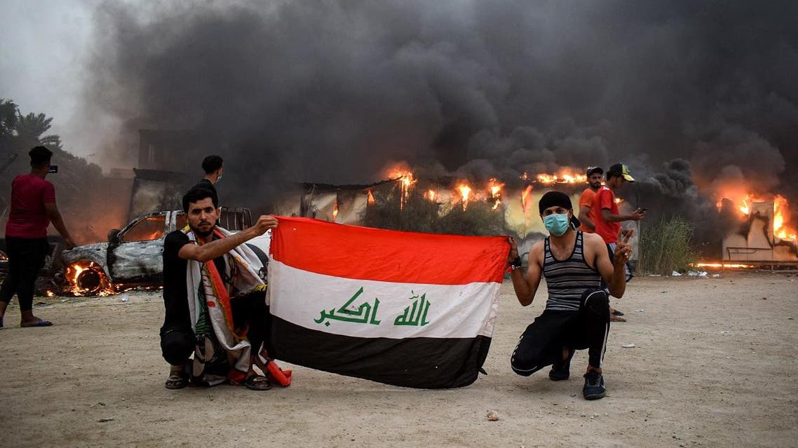 Iraqi protesters pose with a national flag during an anti-government demonstration outside the burning local government headquarters in Nasiriyah. (AFP)