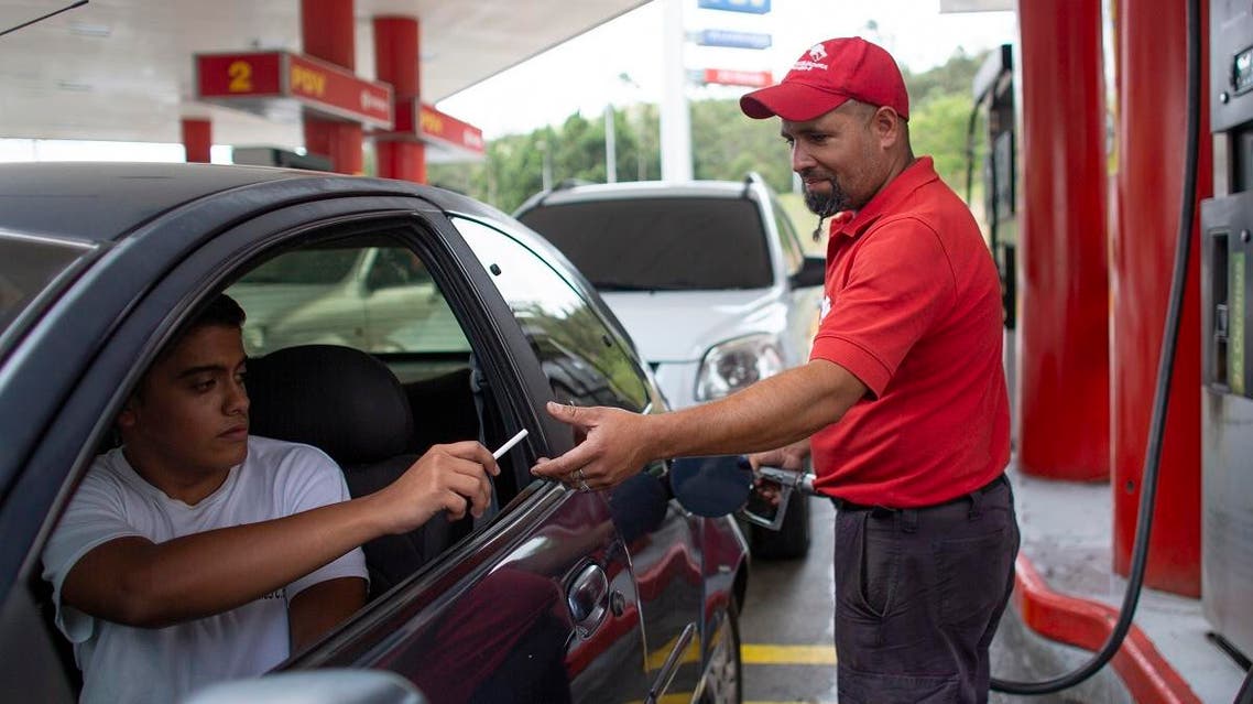 gas station attendant Leowaldo Sanchez takes a cigarette as payment from a motorist as he fills the tank in San Antonio de los Altos. (AP)