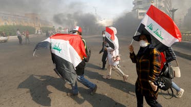 Iraqi demonstrators carry Iraqi flags as they walk at a cloud of smoke during ongoing anti-government protests, in Baghdad, Iraq November 3, 2019. REUTERS