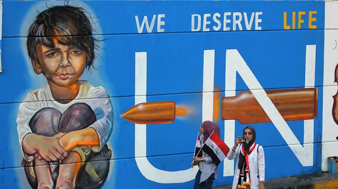 Iraqi demonstrators walk in front of a mural painting in the capital Baghdad's Tahrir square during ongoing anti-government demonstrations on November 13 2019. (AFP)