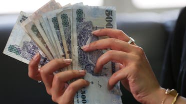 A Saudi woman shows Saudi riyal banknotes at a money exchange shop in Riyadh - Reuters