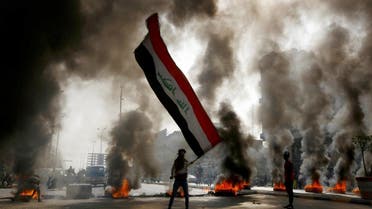 A protester holds an Iraqi flag amid a cloud of smoke from burning tires during ongoing anti-government protests in Najaf, Iraq November 26, 2019. REUTERS