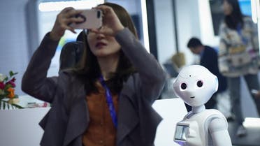 A robot looks at a woman using her mobile phone at China Beijing International High-Tech Expo (CHITEC) in Beijing on October 24, 2019. (AFP)