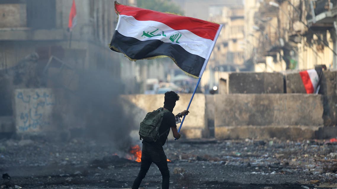 An Iraqi anti-government protester waves a national flag close to a concrete barricade amidst clashes with security forces along the capital Baghdad's Rasheed street near al-Ahrar bridge on November 29, 2019. Iraq's embattled premier announced on November 29 he will resign in keeping with the wishes of the country's top Shiite cleric, after nearly two months of anti-government protests that have cost more than 400 lives.